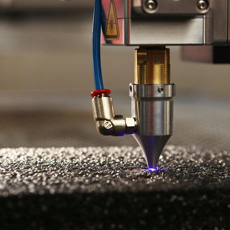 Laser cutting head with a nozzle and glowing beam working on a dark textured surface